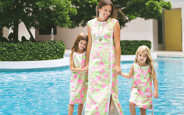 Women holding two little girls' hands wearing matching dresses standing in front of pool